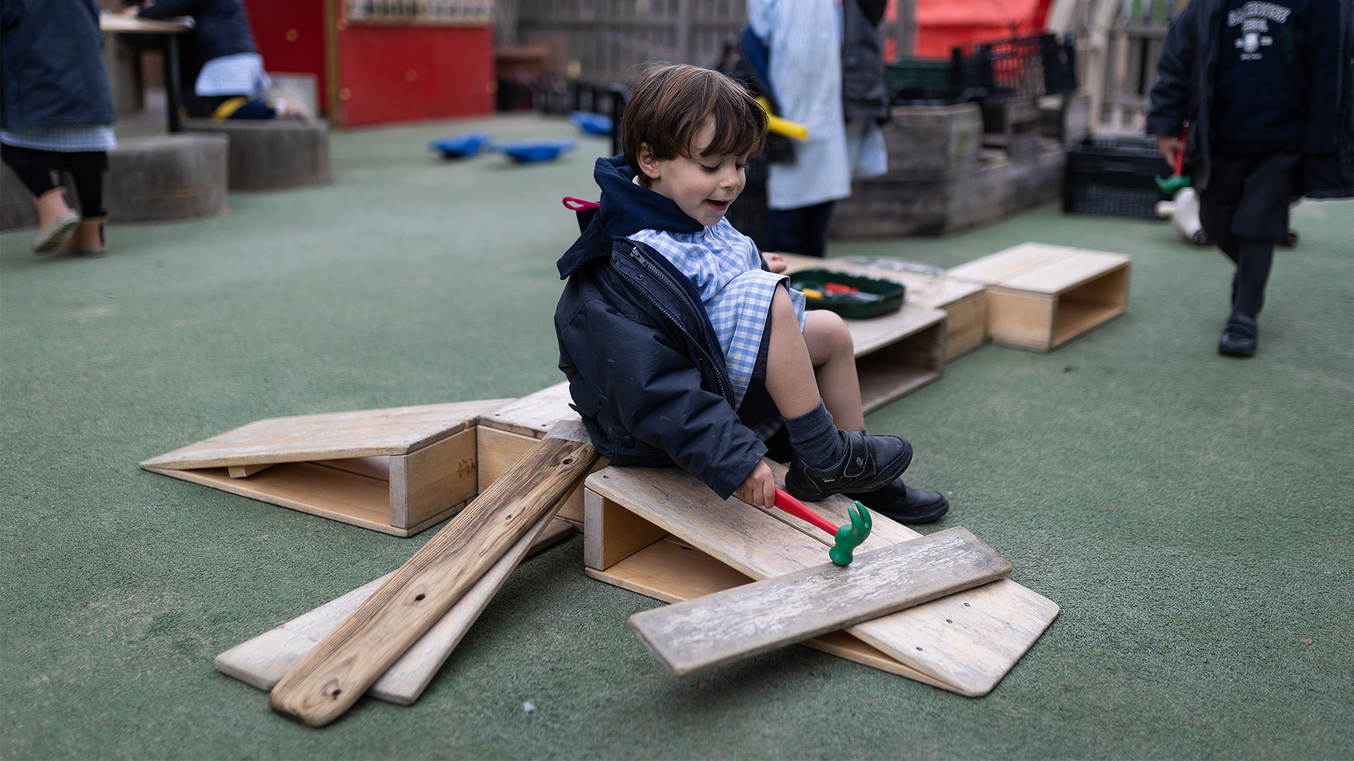 niño jugando con un martillo y una tabla de madera en el patio del colegio